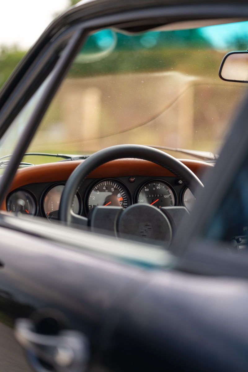 Close up of a black 1976 Porsche 911S Sportomatic interior, showing tan leather dash trim and analog gauges.