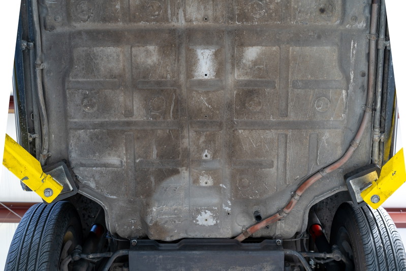 Underside of a black 1976 Porsche 911S Sportomatic on a lift, showing chassis and tire.