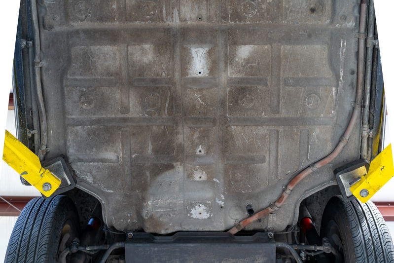 Underside of a black 1976 Porsche 911S Sportomatic on a lift, showing chassis and tire.