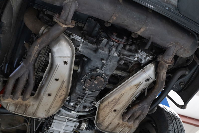 Underside view of a black 1976 Porsche 911S Sportomatic with dual exhaust pipes and engine.
