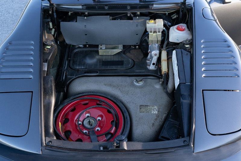 1989 Porsche 930 Turbo Flachbau front trunk with spare tire on red rim.