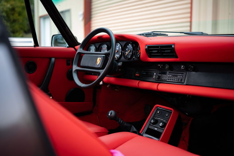 Interior view of a red 1989 Porsche 930 Turbo Flachbau with a black steering wheel and instrument cluster.