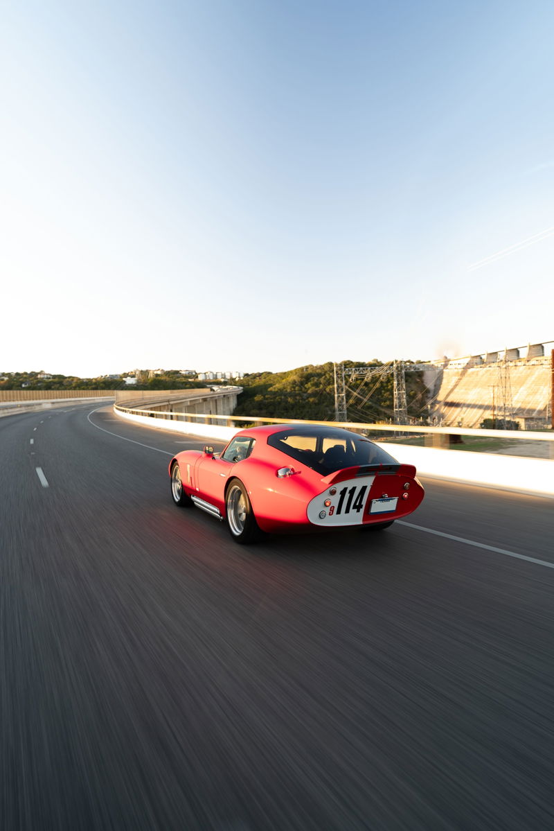 Red 1965 Superformance Shelby Daytona Coupe with racing livery #114 speeds down the track.