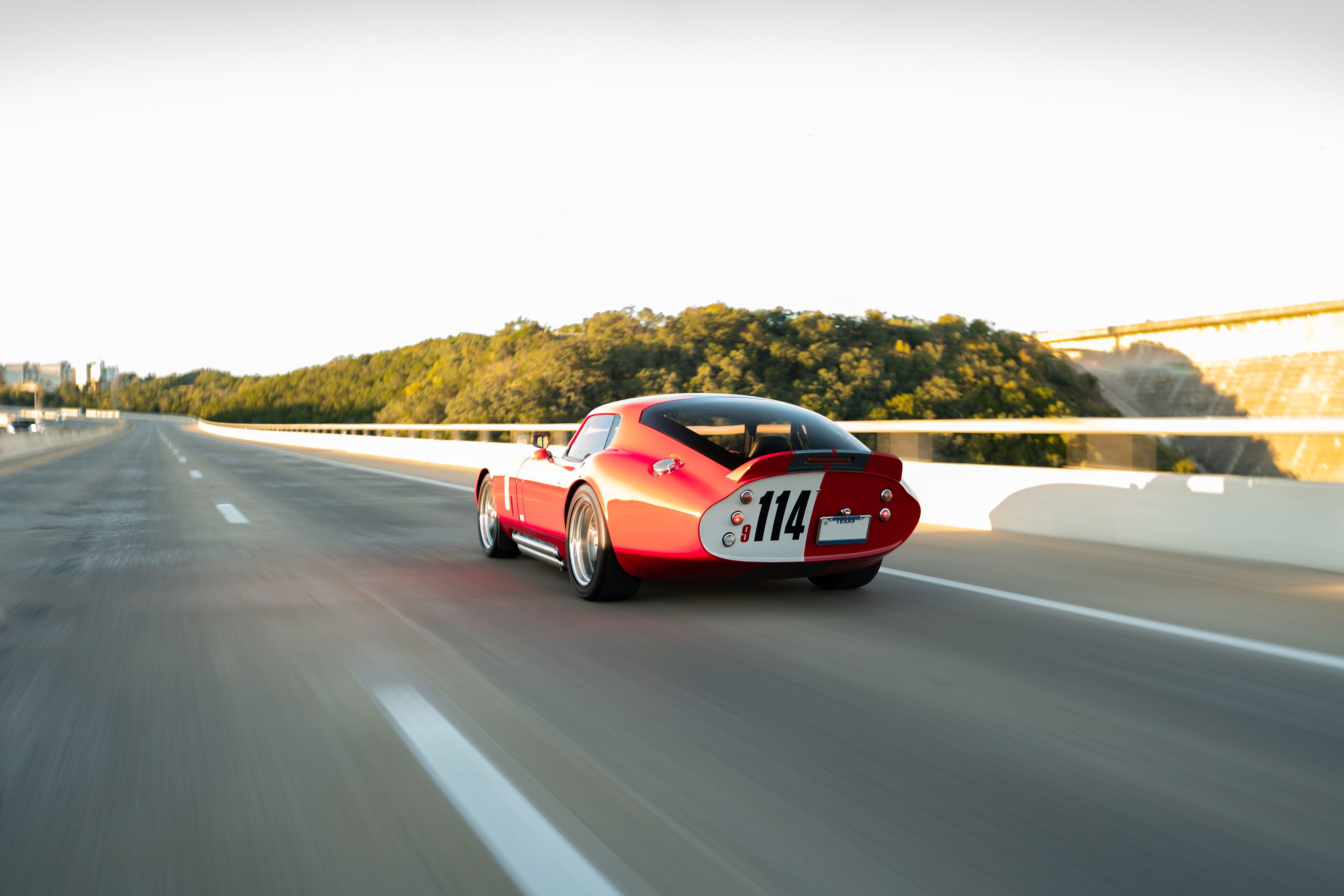 Monza Red 1965 Superformance Shelby Daytona CSX with #114 livery speeds down the highway.