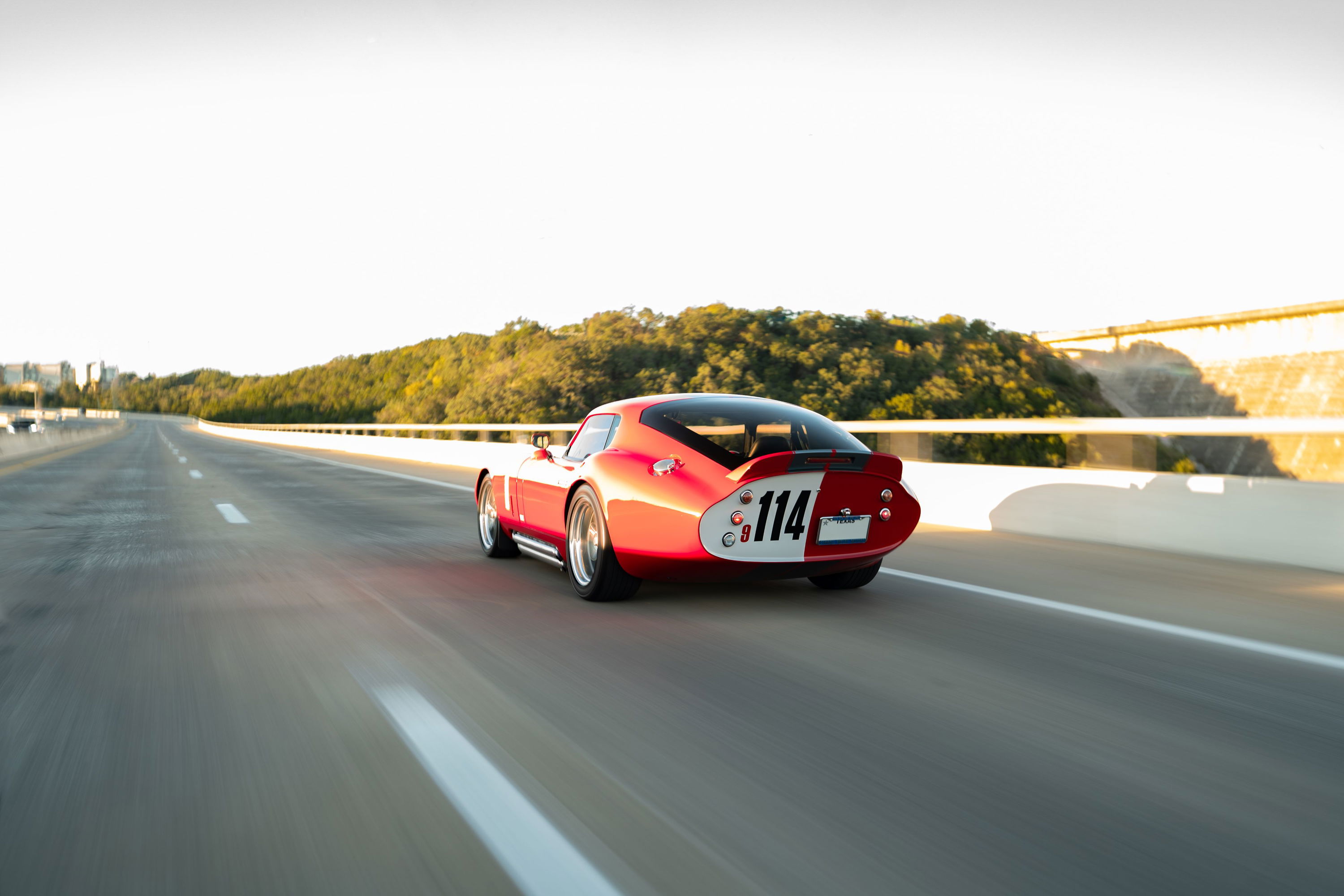 Monza Red 1965 Superformance Shelby Daytona CSX with #114 livery speeds down the highway.