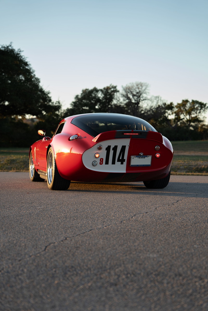 Rear view of a red 1965 Superformance Shelby Daytona Coupe with a racing livery and #114.
