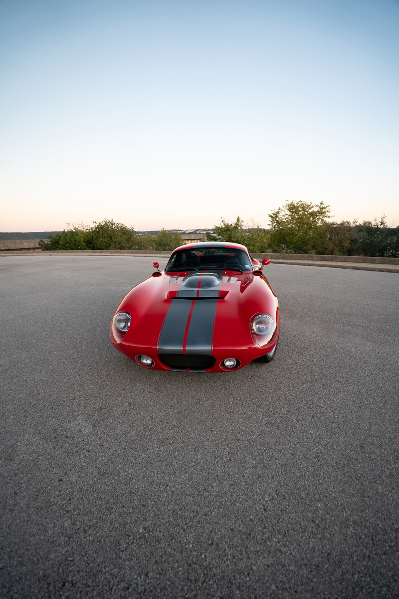 Red 1965 Superformance Shelby Daytona Coupe with dual gray racing stripes and a hood scoop.