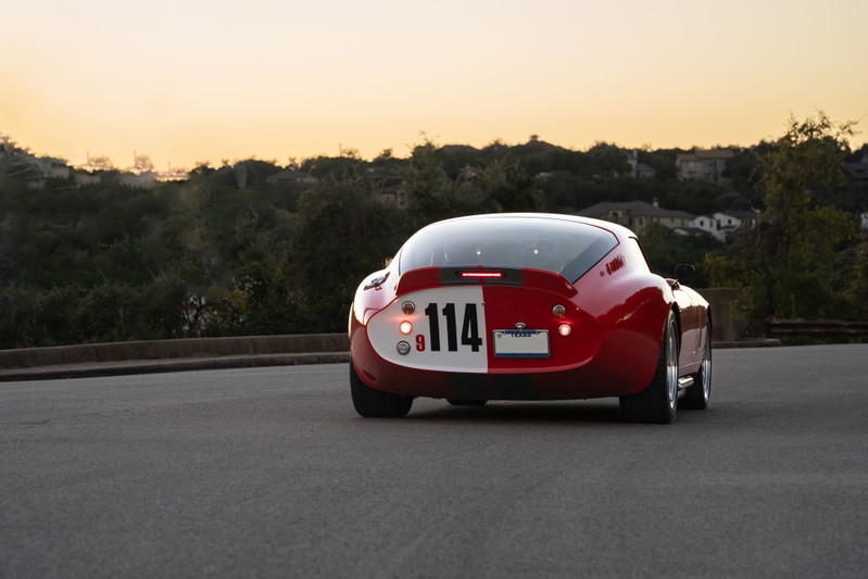 Rear view of a red 1965 Superformance Shelby Daytona coupe with racing livery #114 and chrome rims.