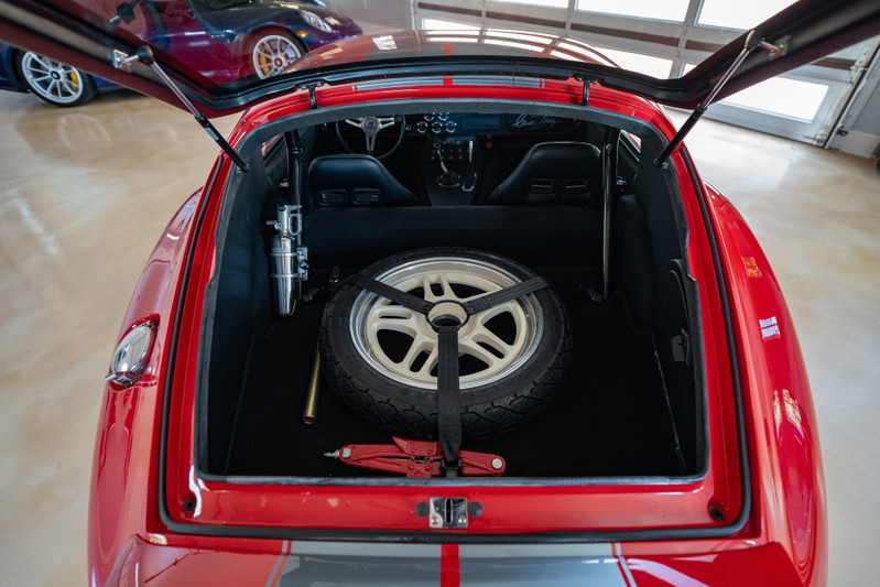 Red 1965 Superformance Shelby Daytona with spare tire, jack, and racing seats in trunk.
