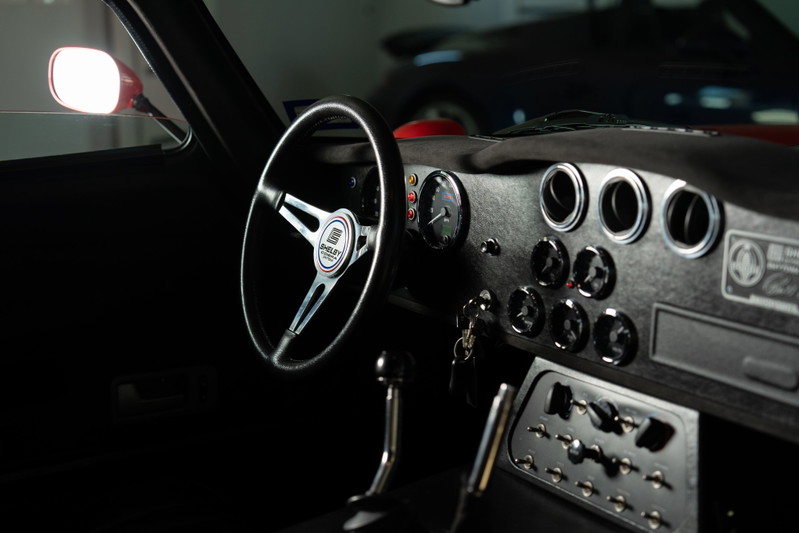 Interior of a Monza Red 1965 Superformance Shelby Daytona CSX, featuring a vintage steering wheel and dashboard gauges.