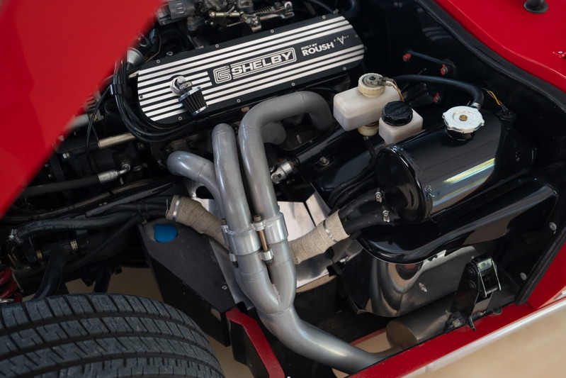 Red 1965 Superformance Shelby Daytona Coupe engine bay, Roush V-engine, chrome exhaust headers, shiny black reservoirs.