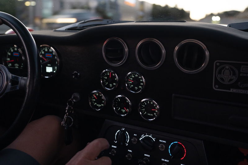 Interior of a Monza Red 1965 Superformance Shelby Daytona CSX, showing dashboard gauges and steering wheel.
