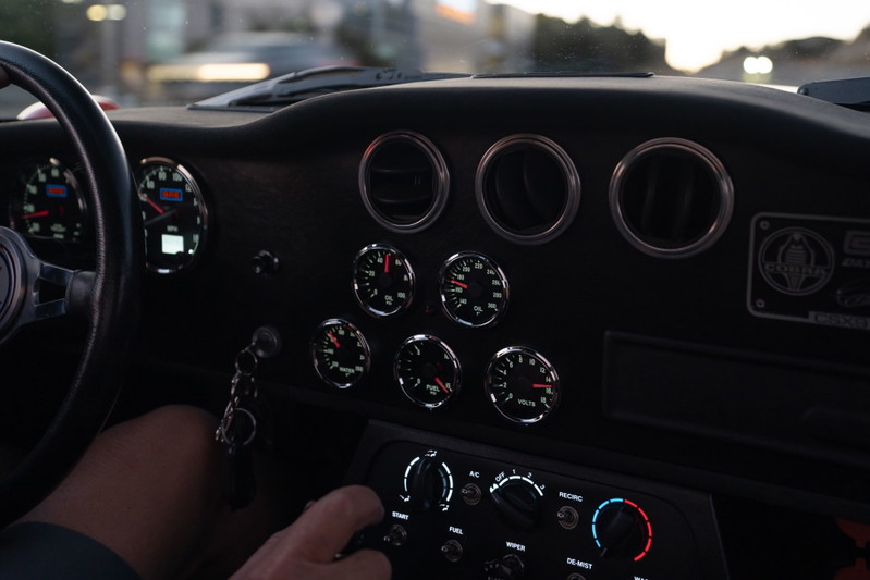 Interior of a Monza Red 1965 Superformance Shelby Daytona CSX, showing dashboard gauges and steering wheel.