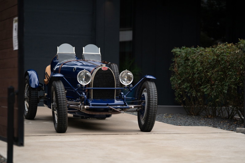 A blue 1927 Bugatti Type 35 Pur Sang roadster with exposed wire wheels and dual windscreens.