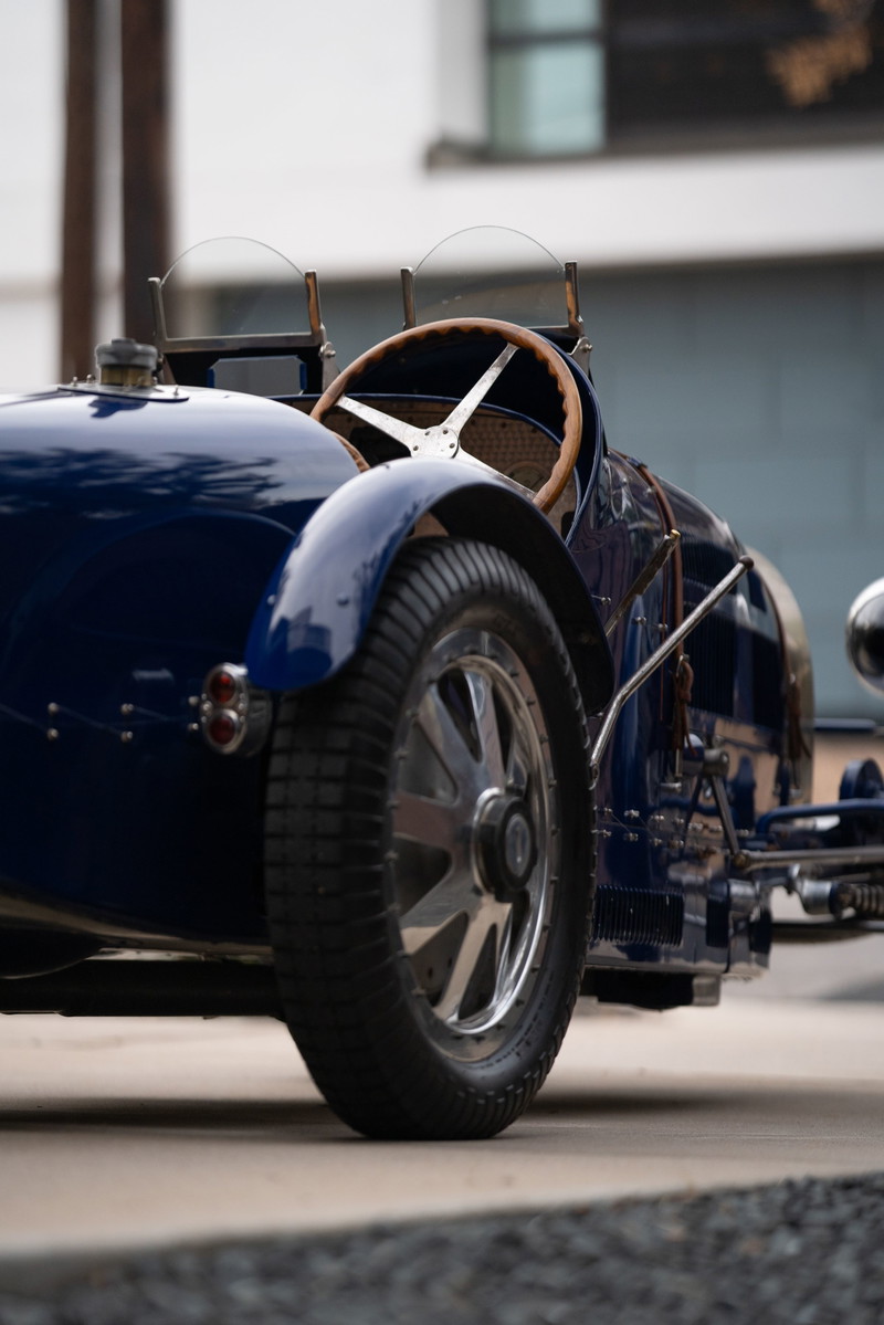 Classic blue 1927 Bugatti Type 35 race car, featuring a wooden steering wheel and wire-spoke rims.