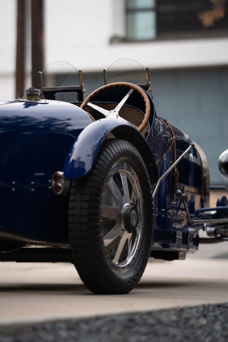 Classic blue 1927 Bugatti Type 35 race car, featuring a wooden steering wheel and wire-spoke rims.