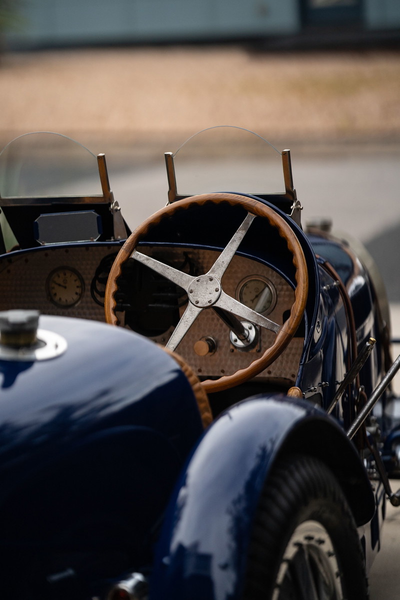 Close-up of a vintage blue 1927 Bugatti Type 35 dashboard with a wooden steering wheel and gauges.