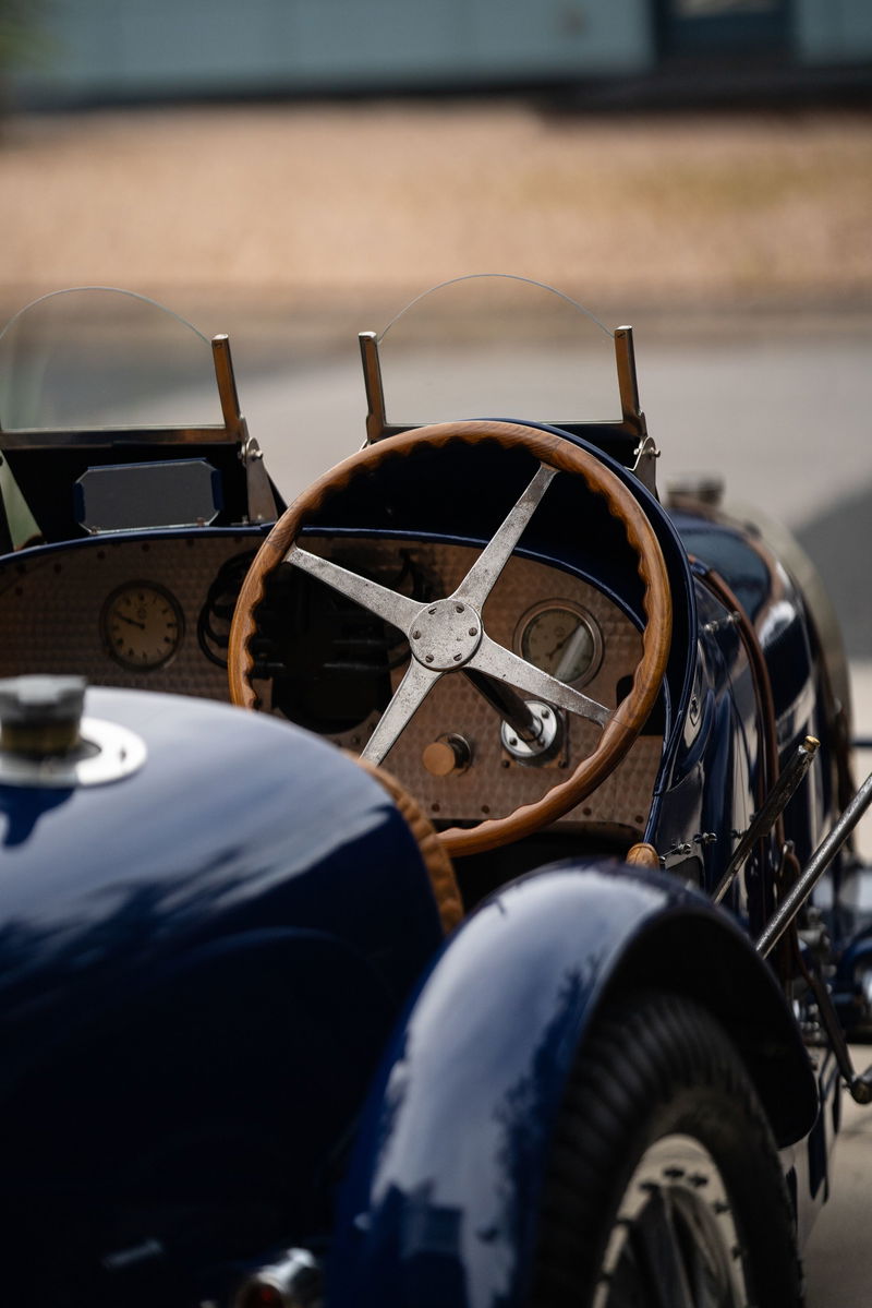 Close-up of a vintage blue 1927 Bugatti Type 35 dashboard with a wooden steering wheel and gauges.