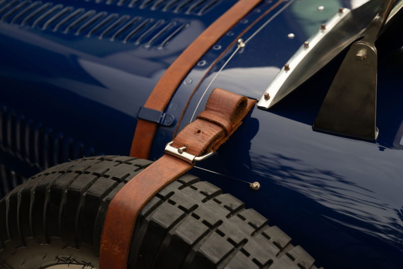 Detail of a blue 1927 Bugatti Type 35's fender, spare tire, and leather hood strap.