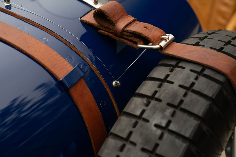 Close-up of a blue 1927 Bugatti Type 35 with leather straps holding a spare tire.