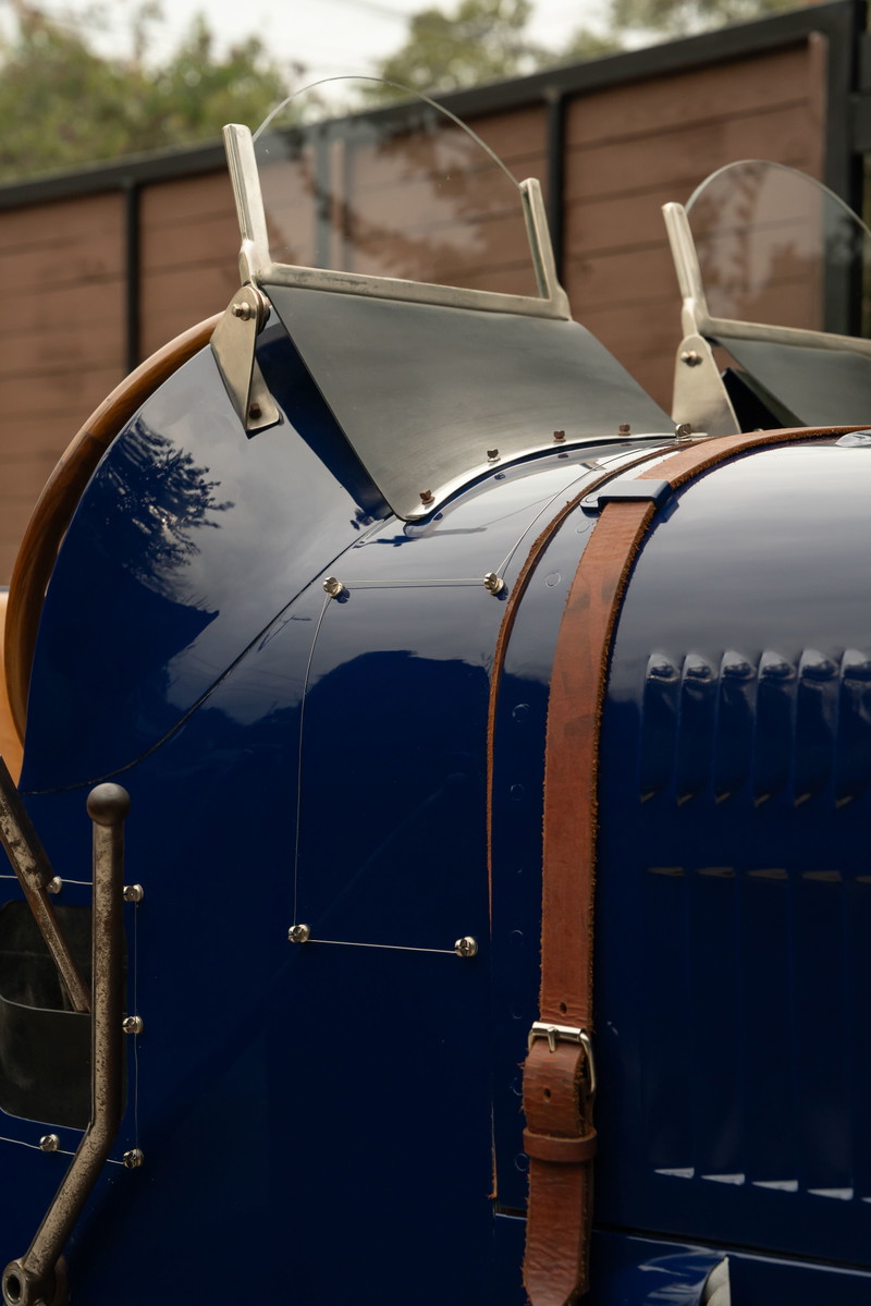 Close-up of a shiny blue 1927 Bugatti Type 35 with twin windscreens & leather straps.