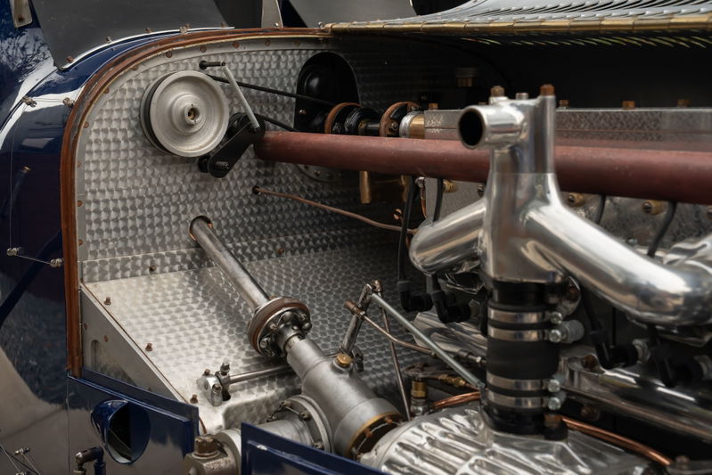 Close-up of the engine bay of a blue 1927 Pur Sang Bugatti Type 35, showing polished metal intake manifold and belt-driven pulley.