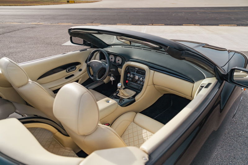 Interior of a black 2003 Aston Martin DB AR1 Zagato convertible with tan quilted leather seats and wood trim.