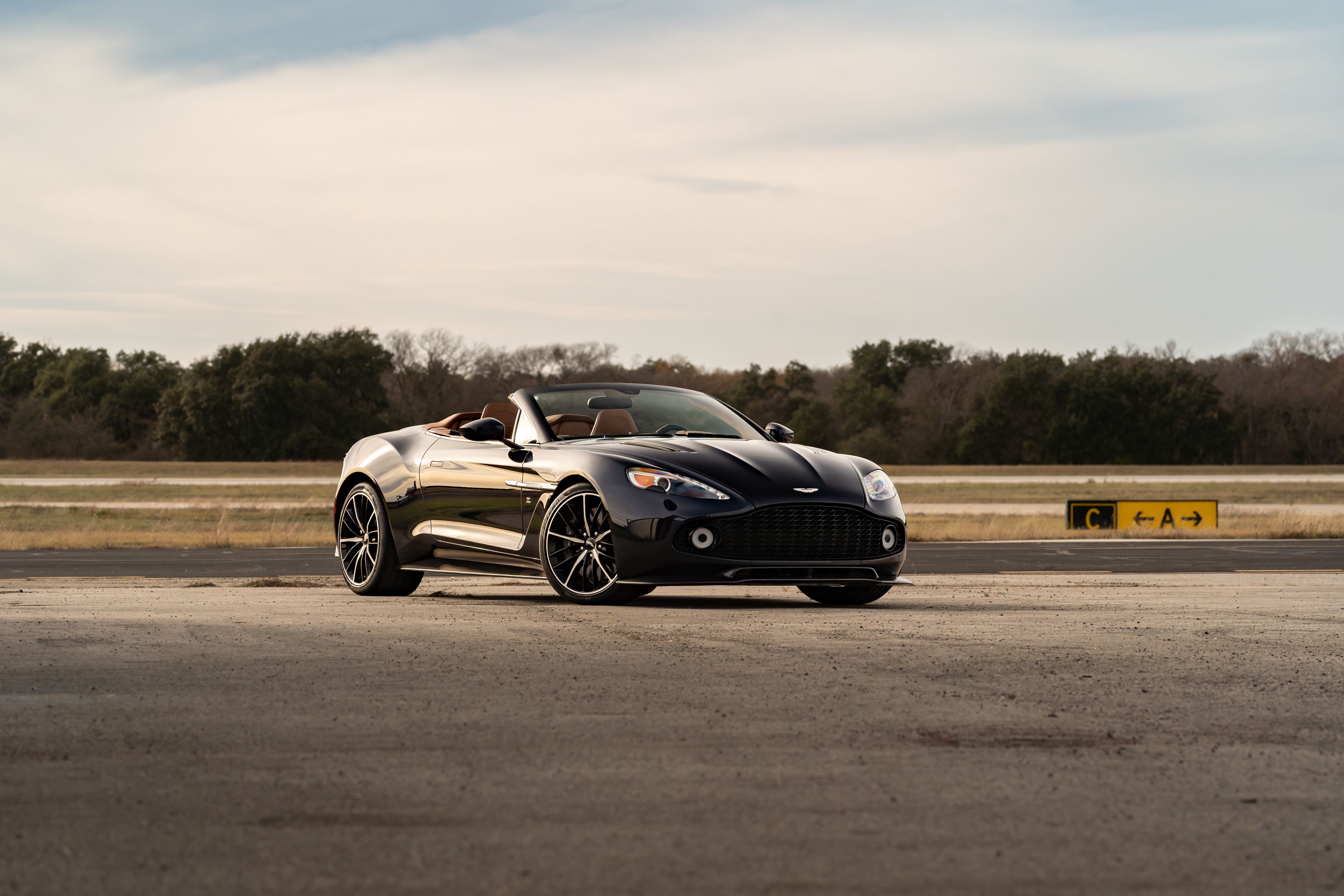 Black 2018 Aston Martin Vanquish Zagato convertible with dark rims on an airfield.