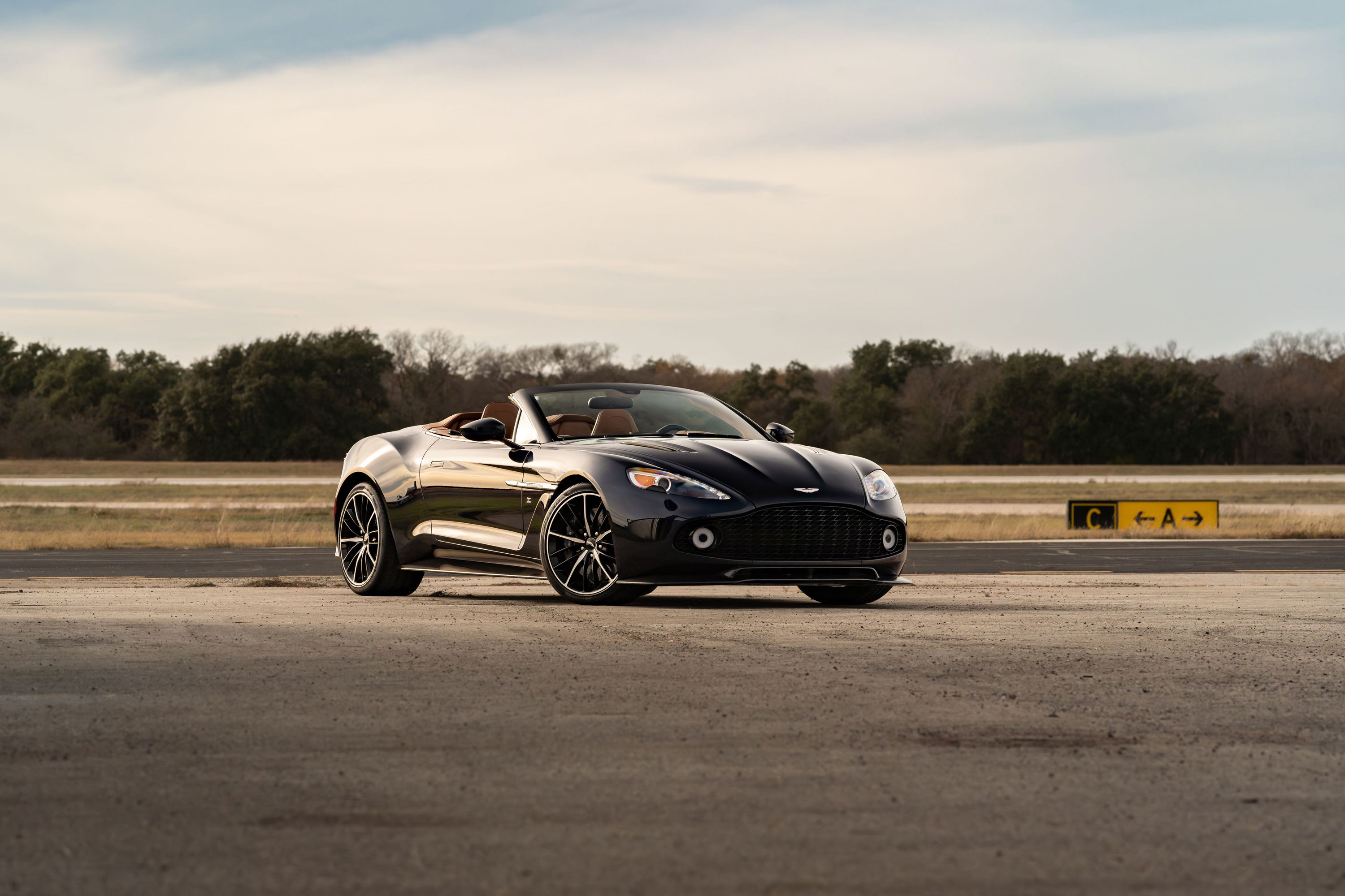 Black 2018 Aston Martin Vanquish Zagato convertible with dark rims on an airfield.