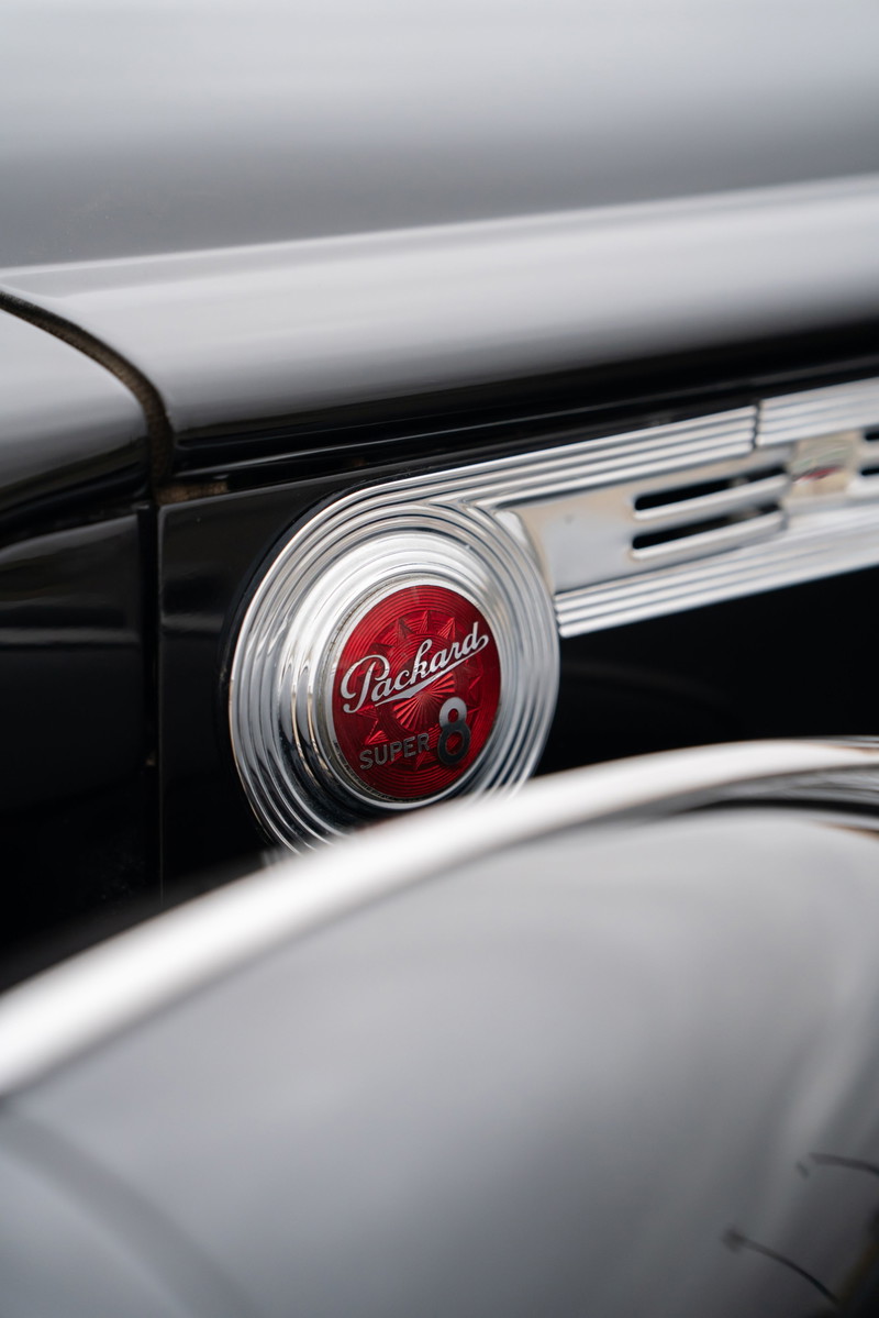 Close-up of a black 1940 Packard Super Eight's circular, red Packard Super 8 emblem and chrome trim.