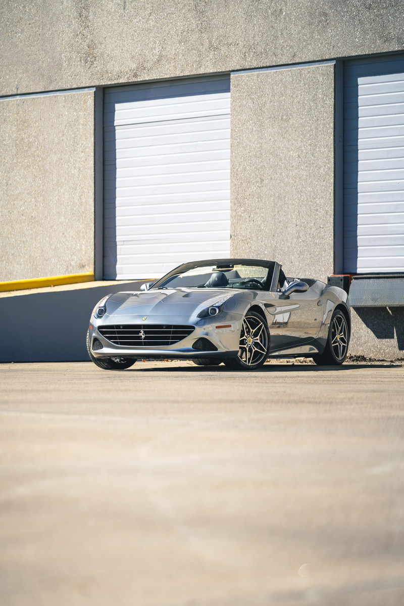 Silver 2016 Ferrari California T convertible with black multi-spoke rims parked outside a building.