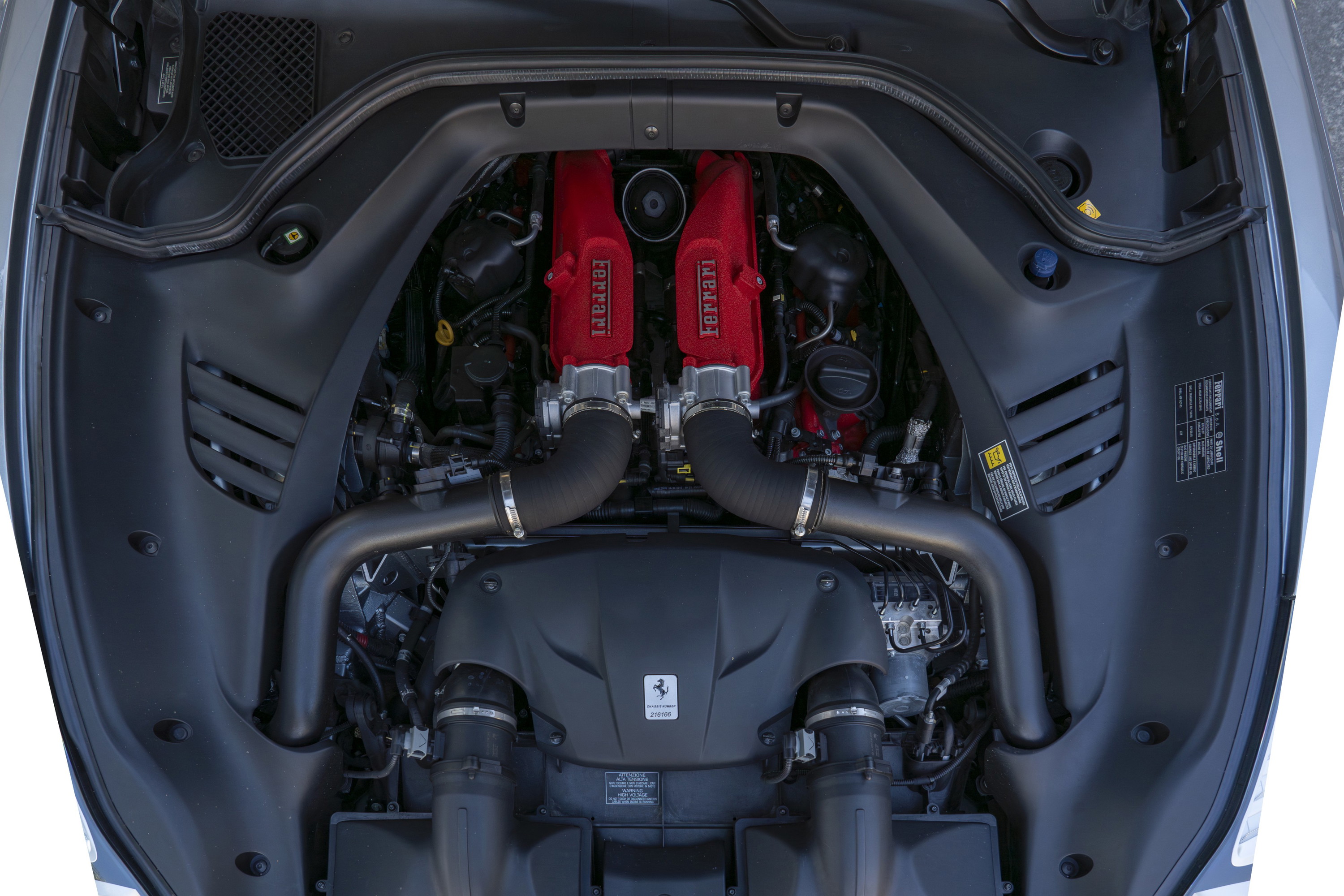 Overhead view of a 2016 Ferrari California T engine bay, showing red Ferrari engine covers and black intake tubes.