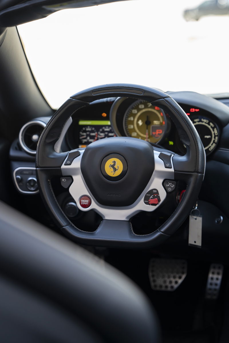 Black leather steering wheel with silver trim and red engine start button in a 2016 Ferrari California T.