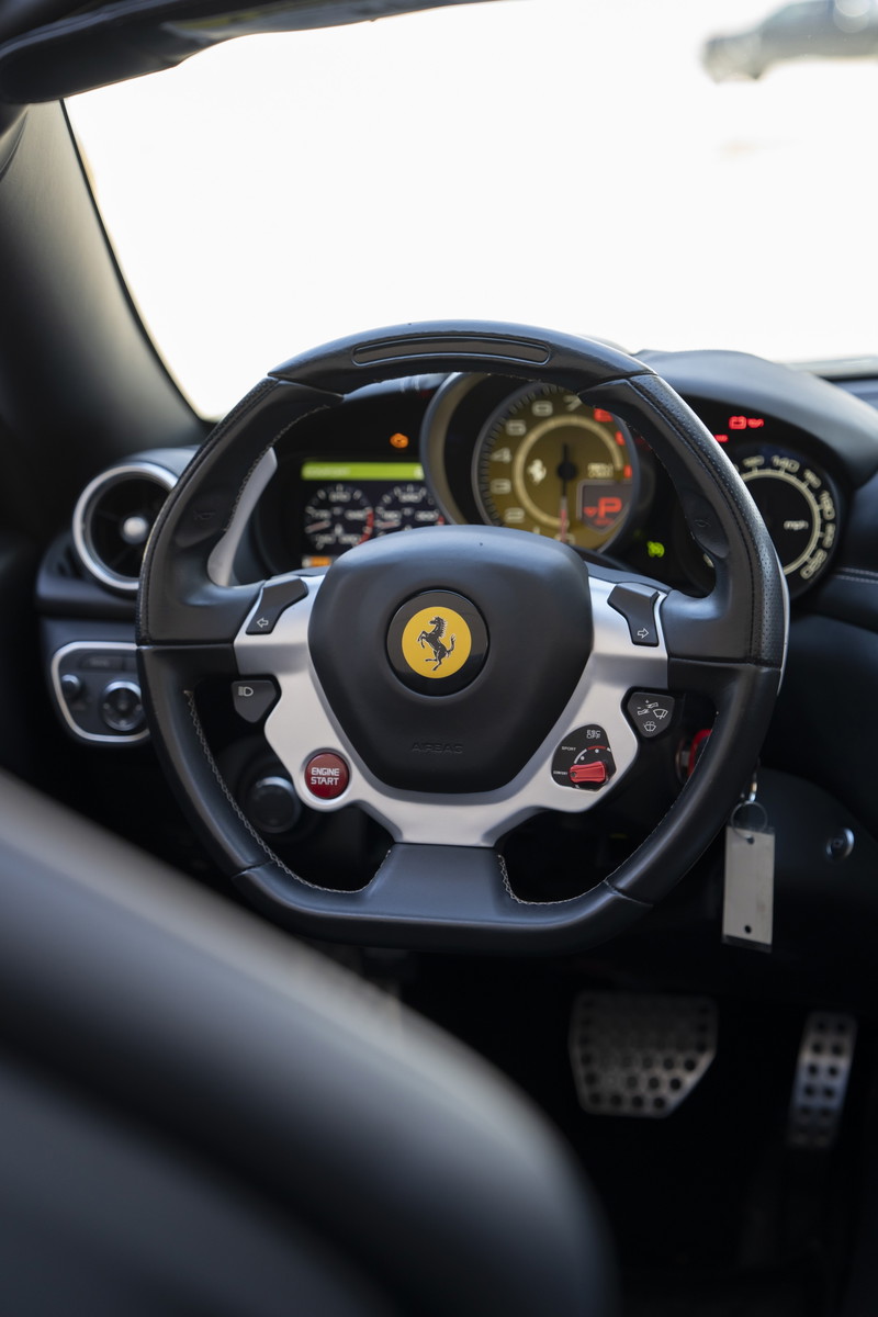 Black leather steering wheel with silver trim and red engine start button in a 2016 Ferrari California T.