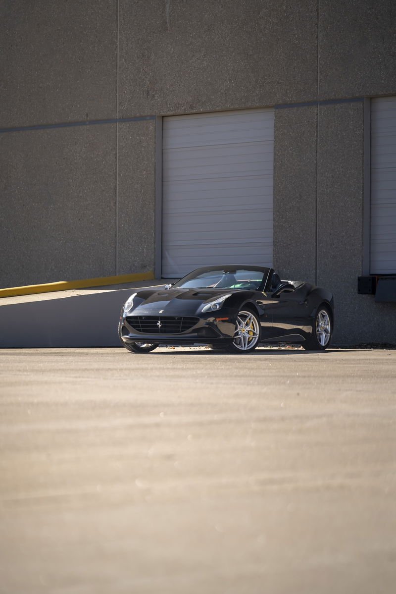 Black 2016 Ferrari California T convertible with silver rims parked outdoors.