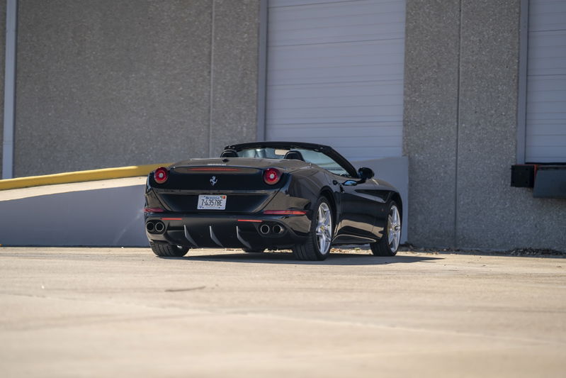 Black 2016 Ferrari California T convertible with silver rims, quad exhaust, and red trim.