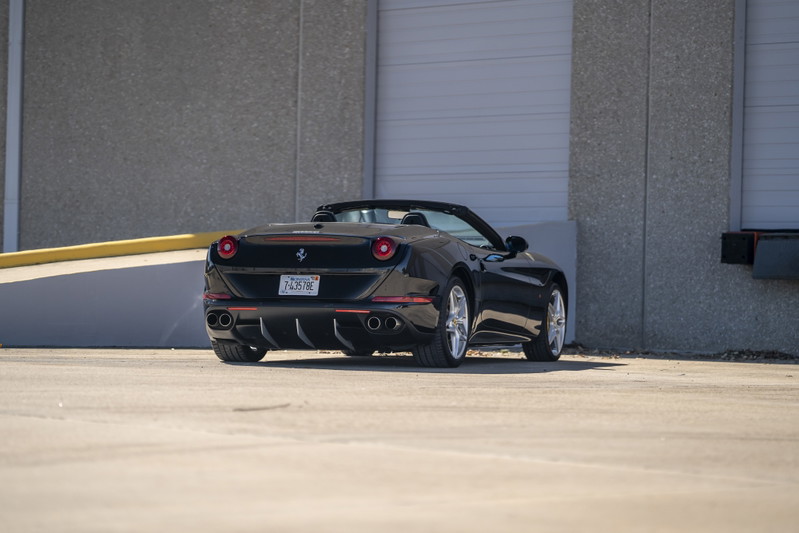 Black 2016 Ferrari California T convertible with silver rims, quad exhaust, and red trim.