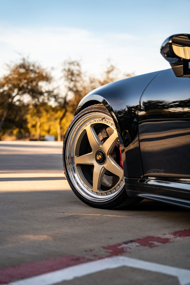 Close up of a black 2023 Porsche 911 Carrera 4 GTS wheel with gold multi-spoke rims.