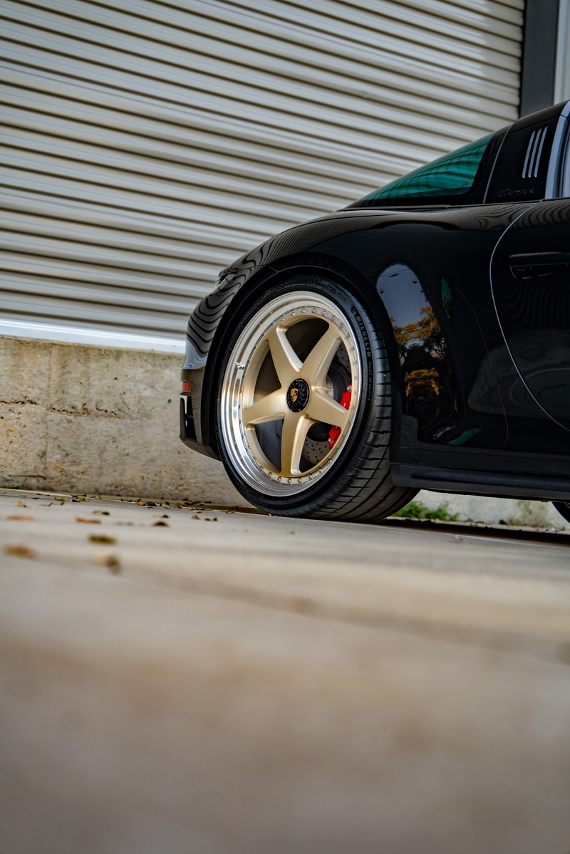 Black 2023 Porsche 911 Carrera 4 GTS with gold five-spoke rims and red brake calipers.