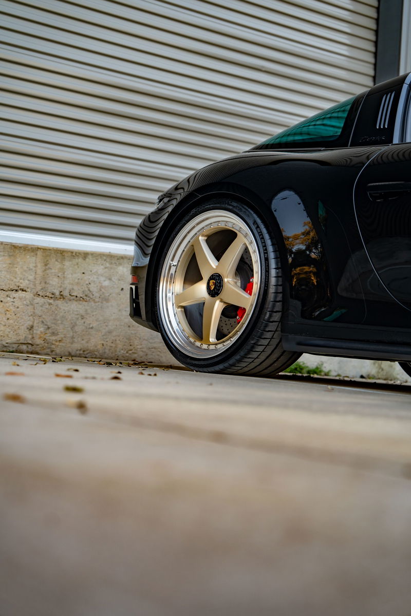 Black 2023 Porsche 911 Carrera 4 GTS with gold five-spoke rims and red brake calipers.