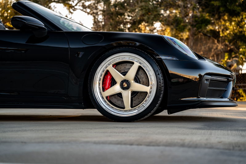 Close-up of a black 2023 Porsche 911 Carrera 4 GTS with gold five-spoke rims and red brake calipers.