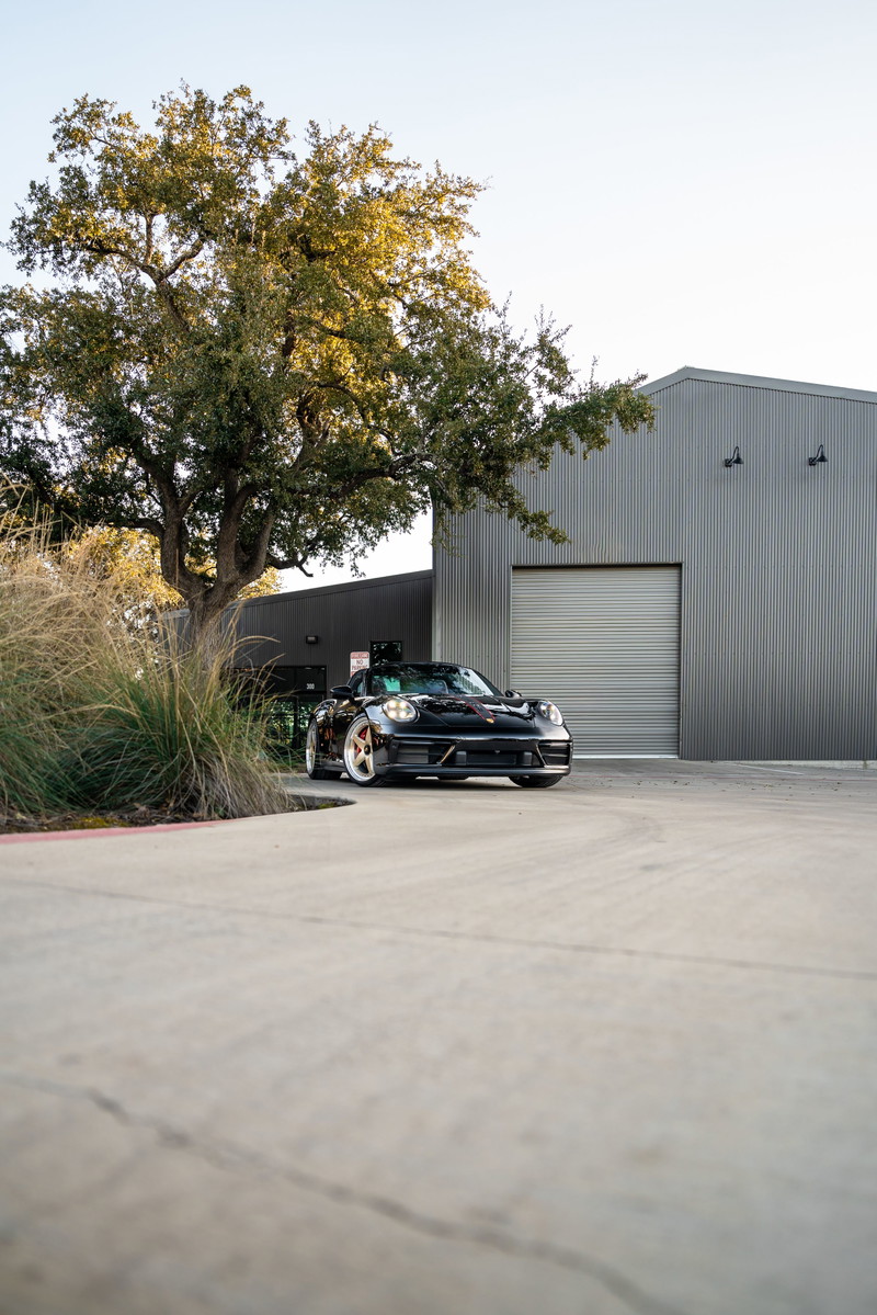 Black 2023 Porsche 911 Carrera 4 GTS with gold rims parked outside a modern building.