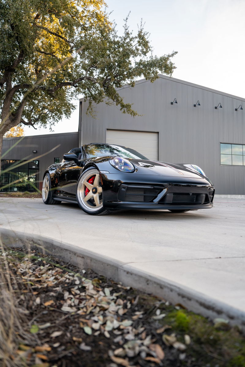 Black 2023 Porsche 911 Carrera 4 GTS convertible with gold rims and red brake calipers.