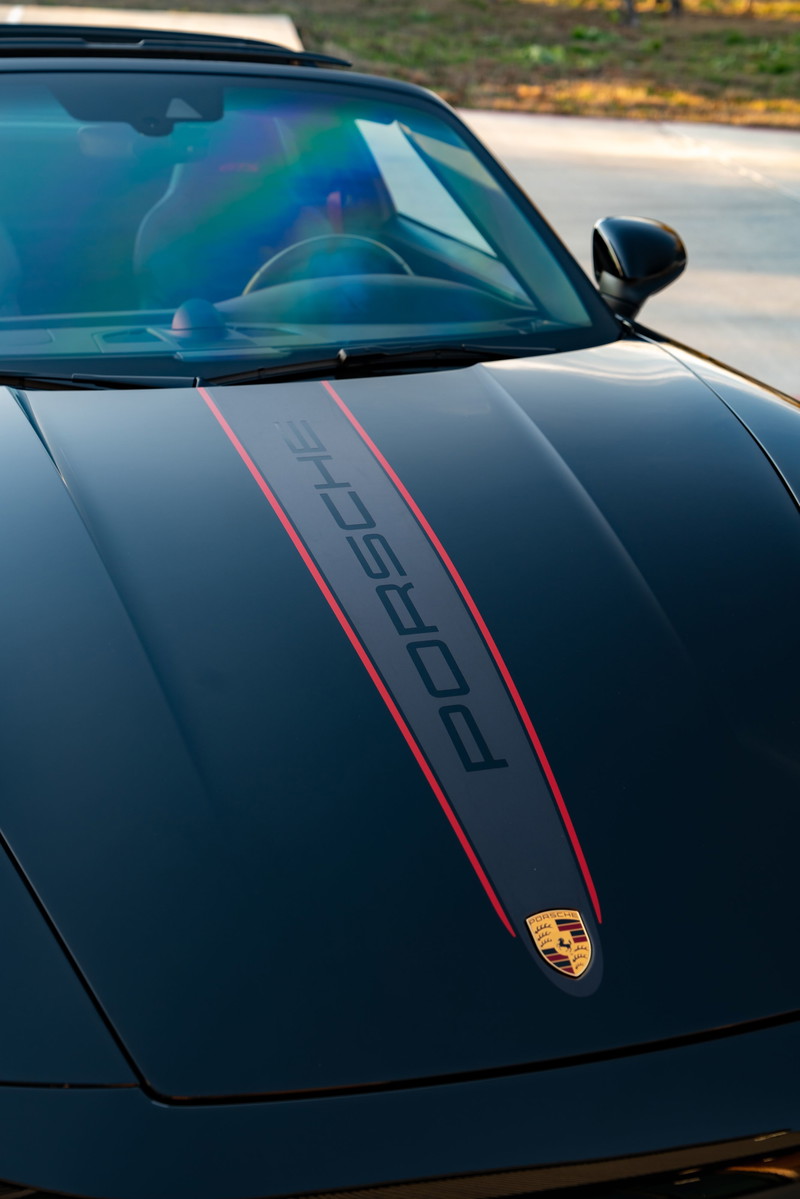 Black 2023 Porsche 911 Carrera 4 GTS hood with central stripe and Porsche crest.