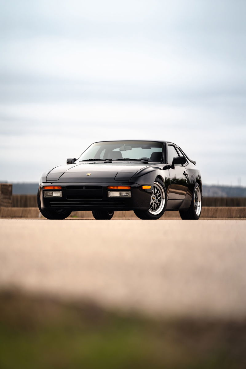 Black 1986 Porsche 944 Turbo with aftermarket rims parked outdoors.