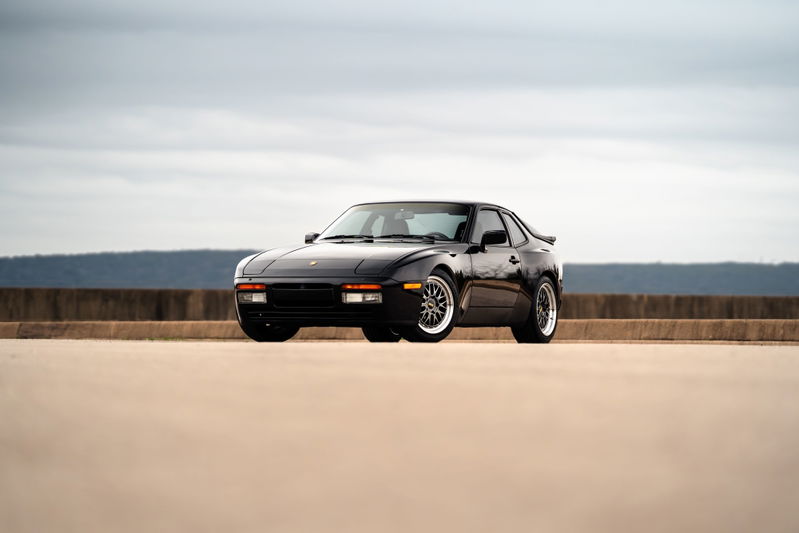 Front 3/4 view of a black 1986 Porsche 944 Turbo with chrome rims.