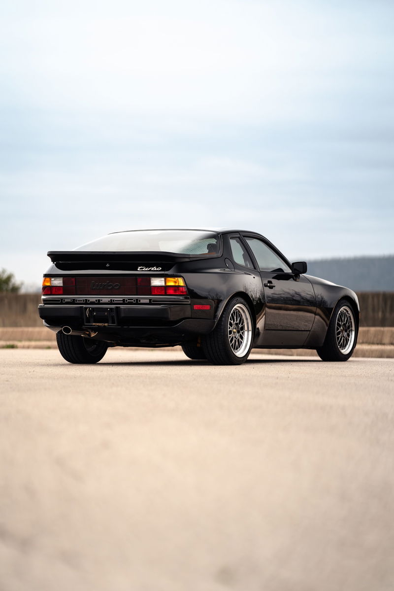Rear view of a black 1986 Porsche 944 Turbo with chrome mesh rims.