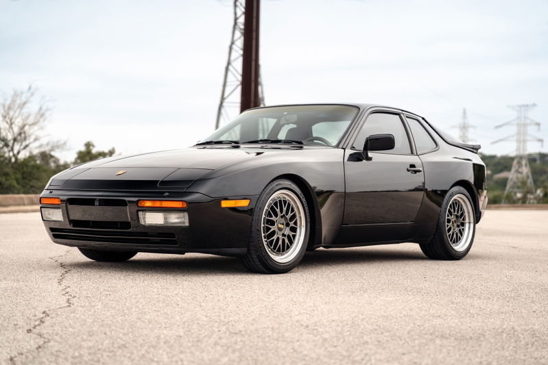 Black 1986 Porsche 944 Turbo with aftermarket BBS rims and a rear spoiler.
