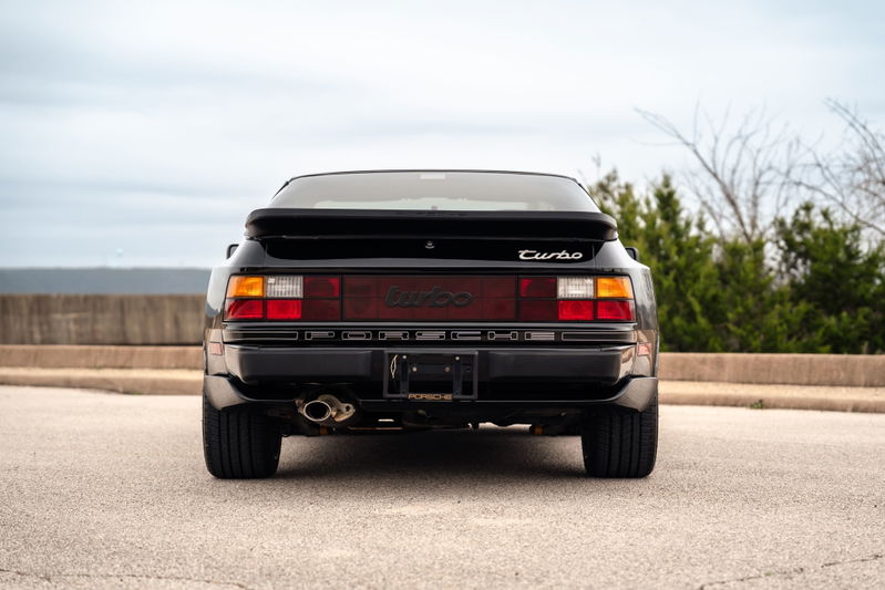 Rear view of a black 1986 Porsche 944 Turbo, showcasing its taillights, exhaust, and turbo badging.
