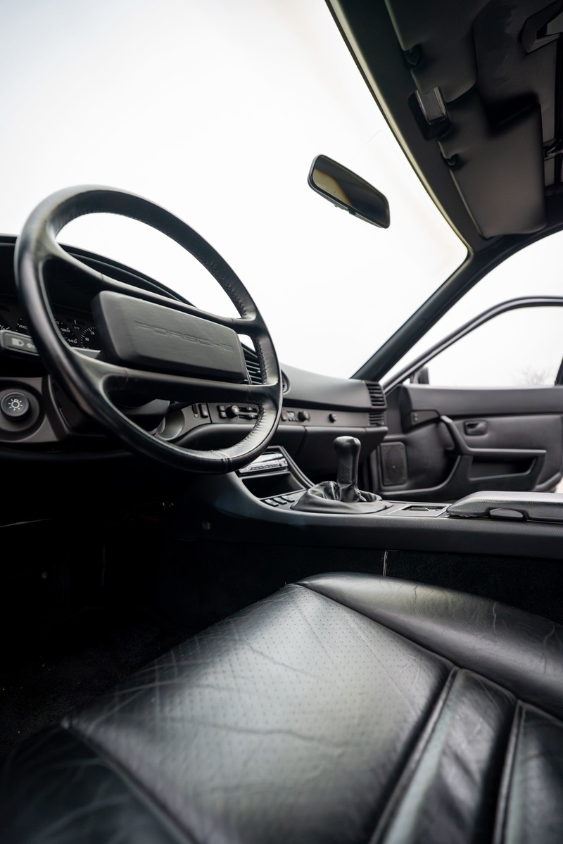 Interior of a black 1986 Porsche 944 Turbo, showing leather seats, steering wheel, and shifter.